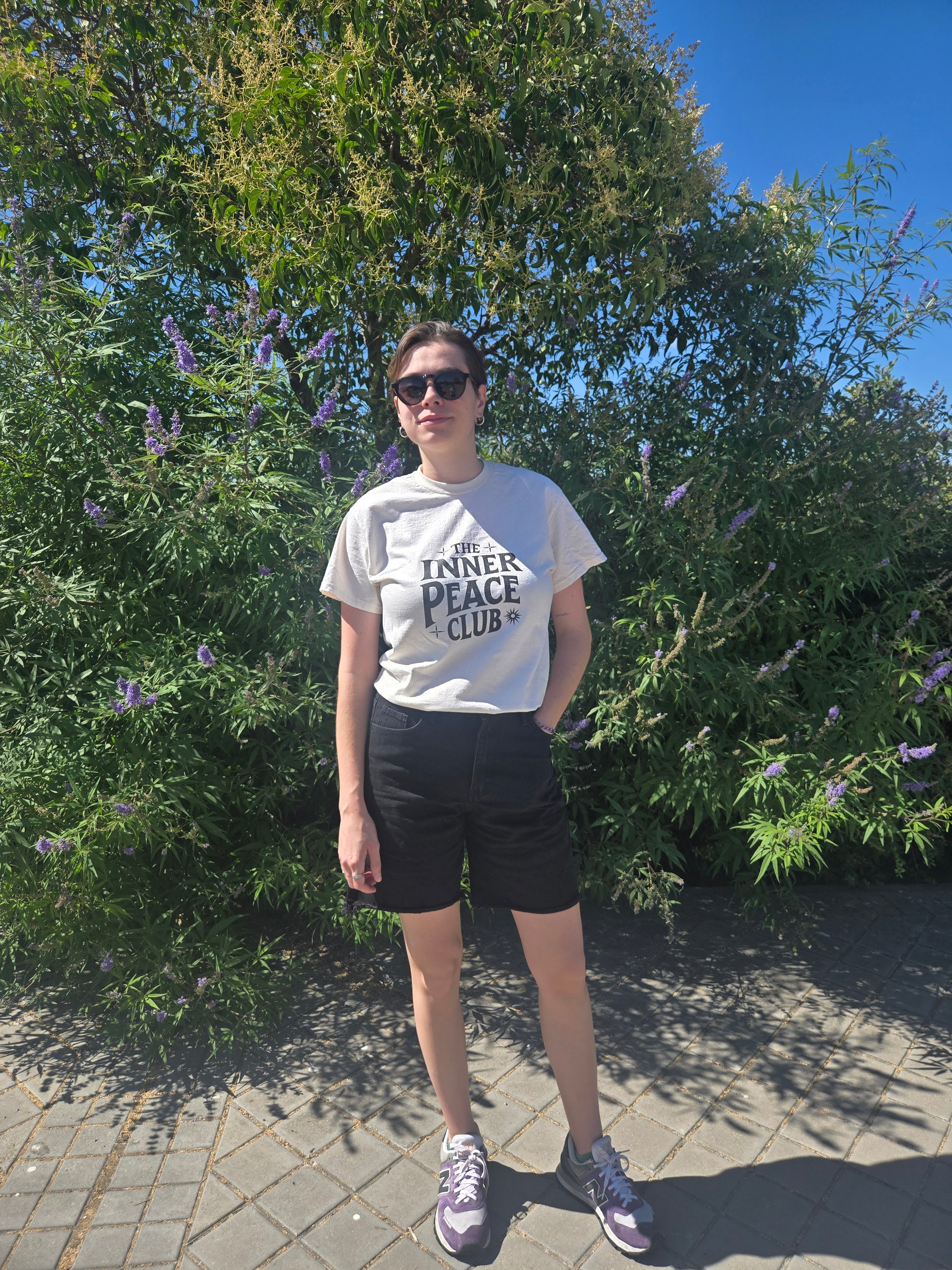 Person wearing a white t-shirt with text, standing outdoors on a sunny day.