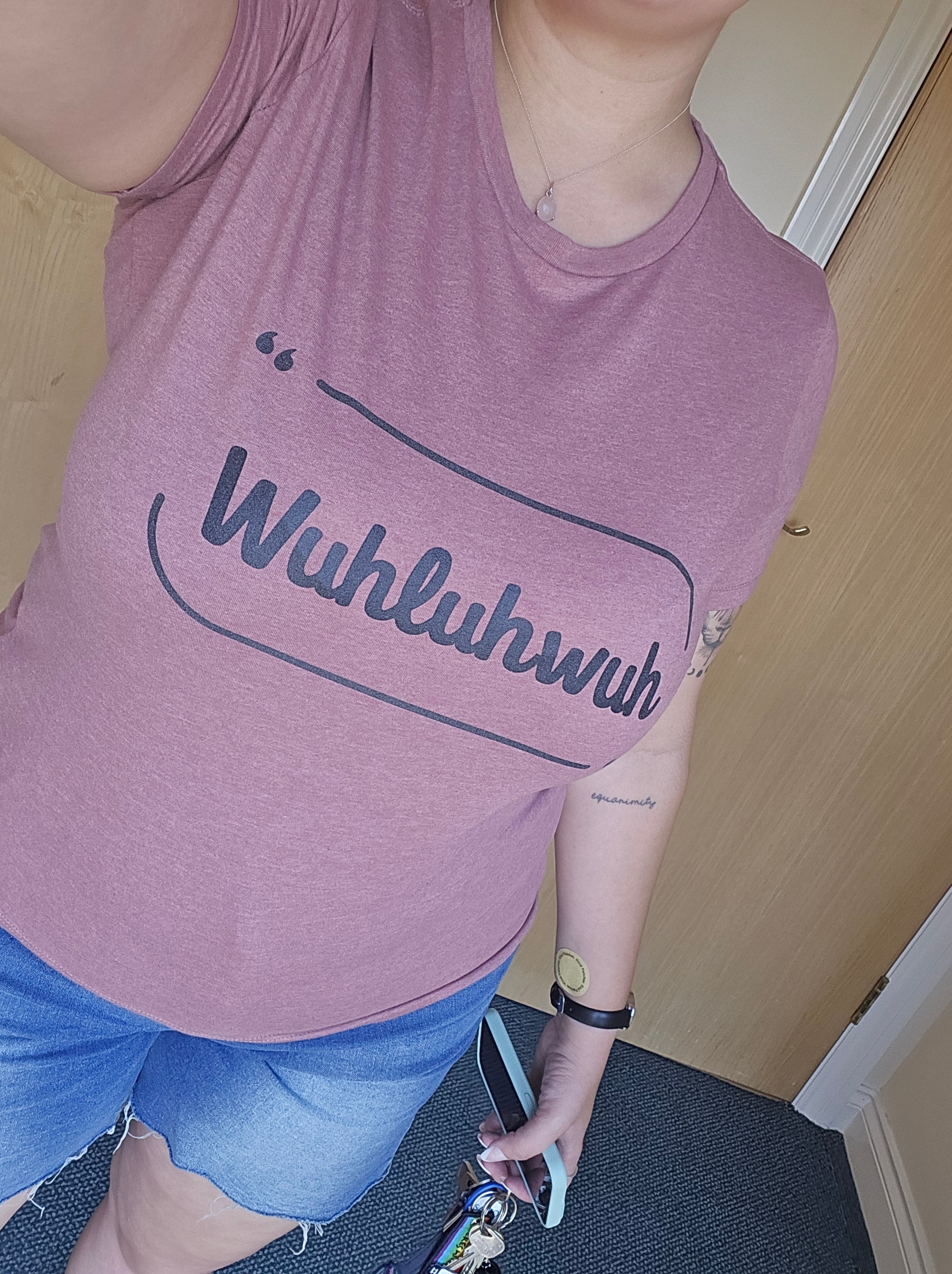 Person wearing a pink tank top with text, standing indoors on a wooden floor.