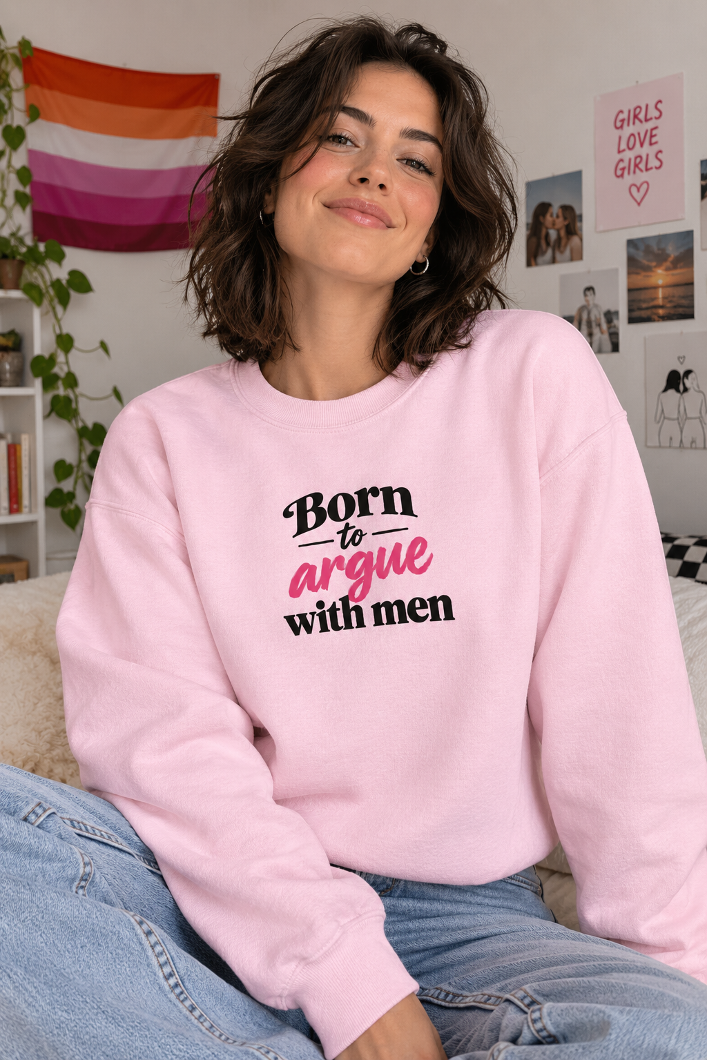 A woman wearing a light pink crewneck sweatshirt with the text 'Born to argue with men' in black and pink lettering, paired with light blue jeans in a cozy indoor setting.