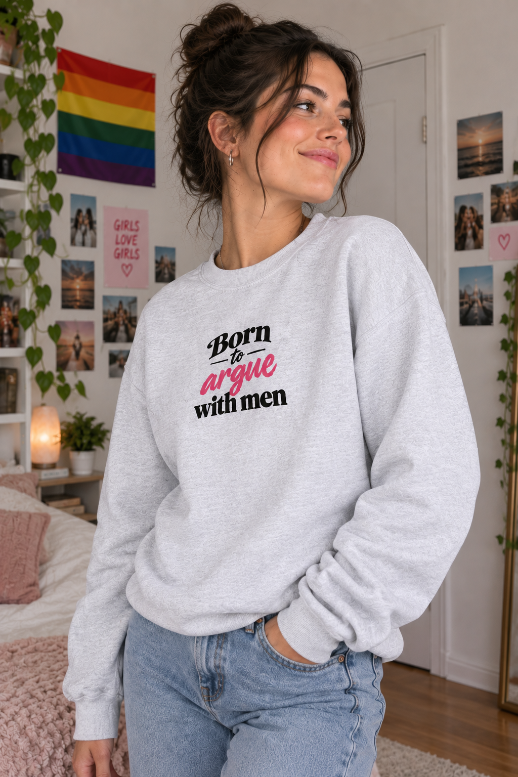 A woman wearing a light gray crewneck sweatshirt with the text 'Born & argue with men' in black and pink, paired with light blue jeans in a decorated bedroom setting.
