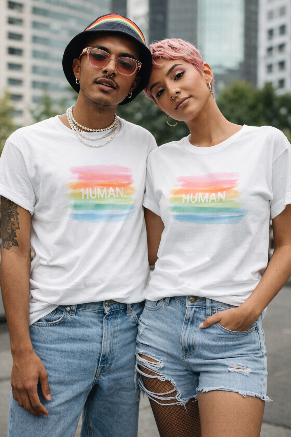 Two people wearing white t-shirts with a rainbow-colored 'HUMAN' graphic, standing outdoors.