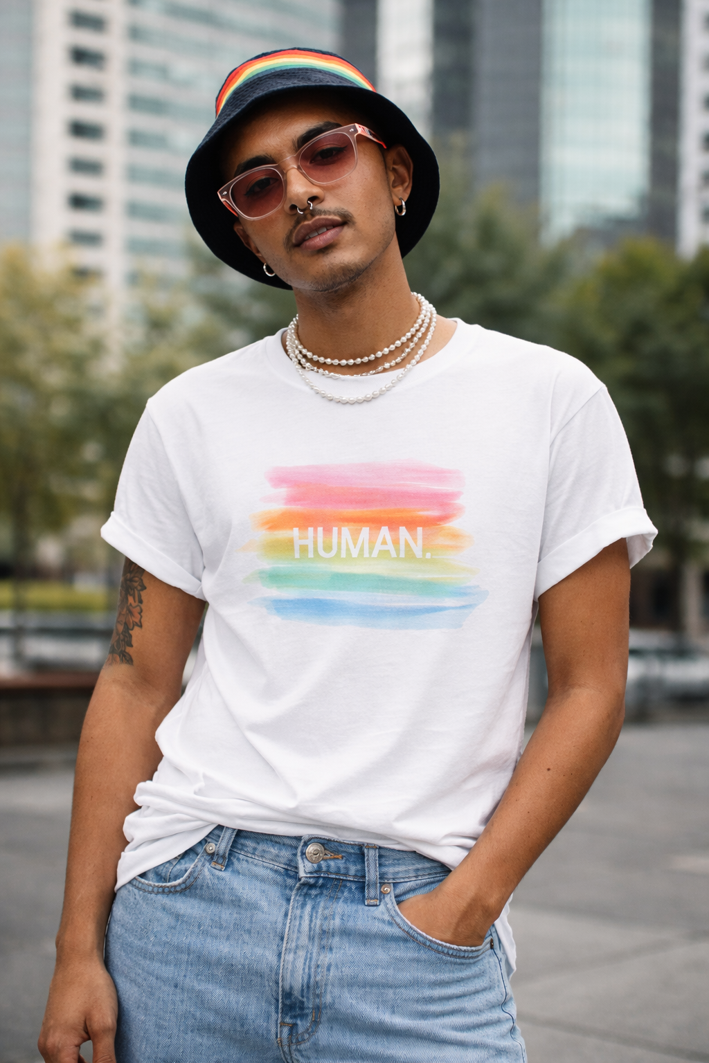 Person wearing a white t-shirt with a rainbow-colored 'HUMAN' design, standing in an urban setting.