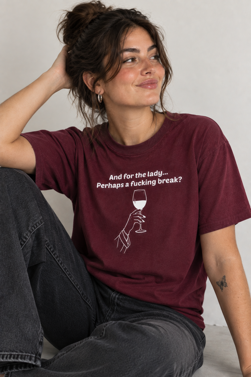 A woman wearing a maroon crewneck graphic t-shirt with the text 'And for the lady.