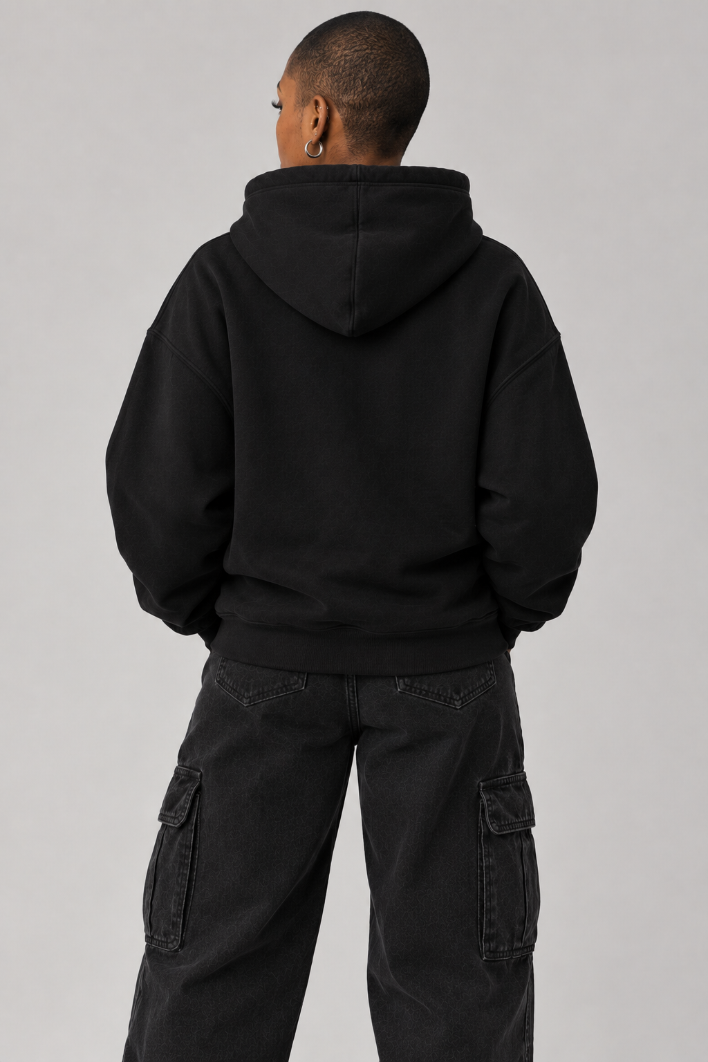 A person shown from the back wearing a black pullover hoodie and black cargo pants against a plain light gray studio background.