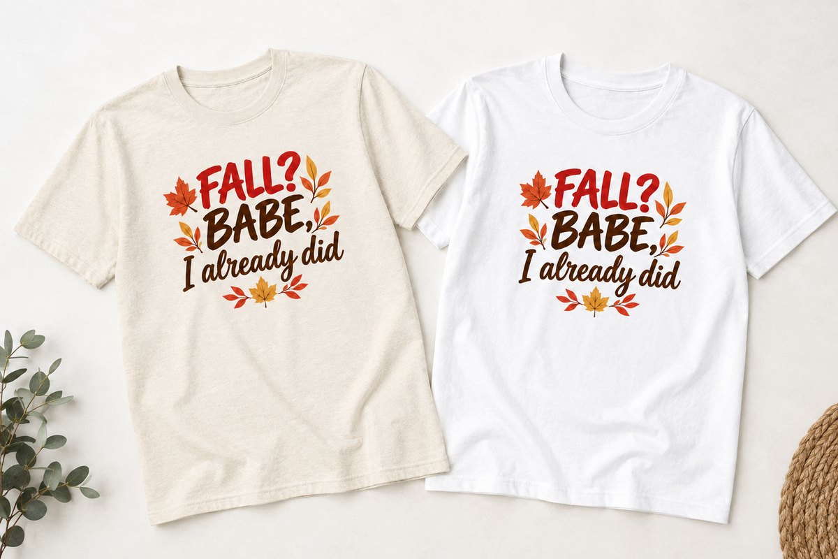 Two short-sleeve graphic T-shirts laid flat on a light background. One shirt is warm off-white/cream and the other is white, both printed with the phrase “FALL? BABE, I already did” in red and brown lettering with orange and yellow autumn leaves.