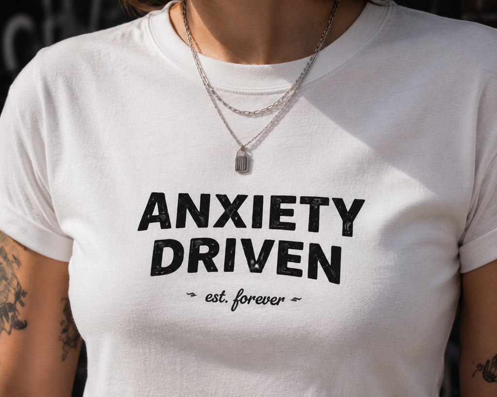 A close-up of a person wearing a white short-sleeve T-shirt with bold black text reading 'ANXIETY DRIVEN' and smaller script text 'est. forever' underneath.
