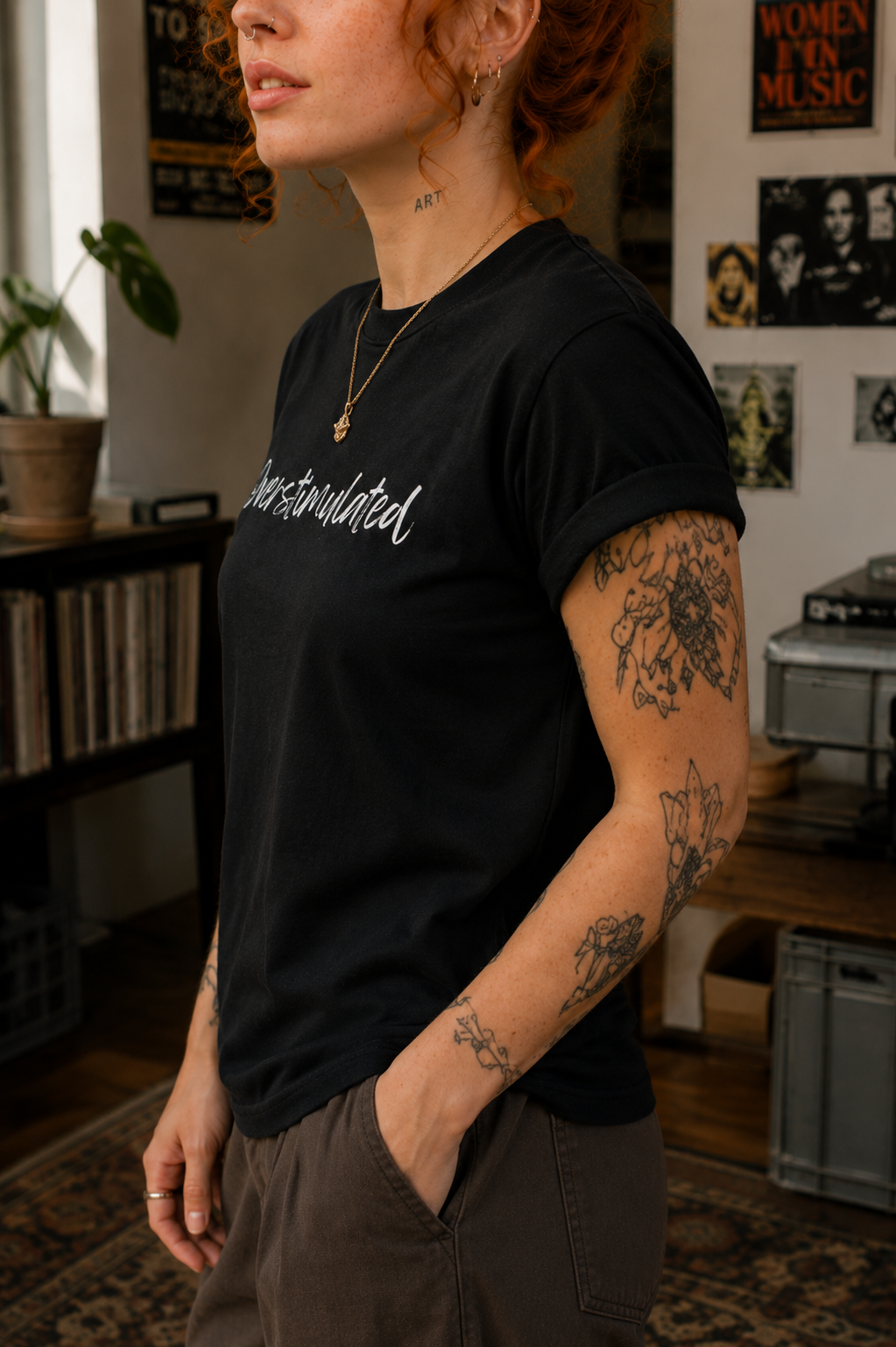 A woman wearing a black short-sleeve t-shirt with white cursive text that reads 'unrestricted' across the chest, standing in a room with posters and records in the background.