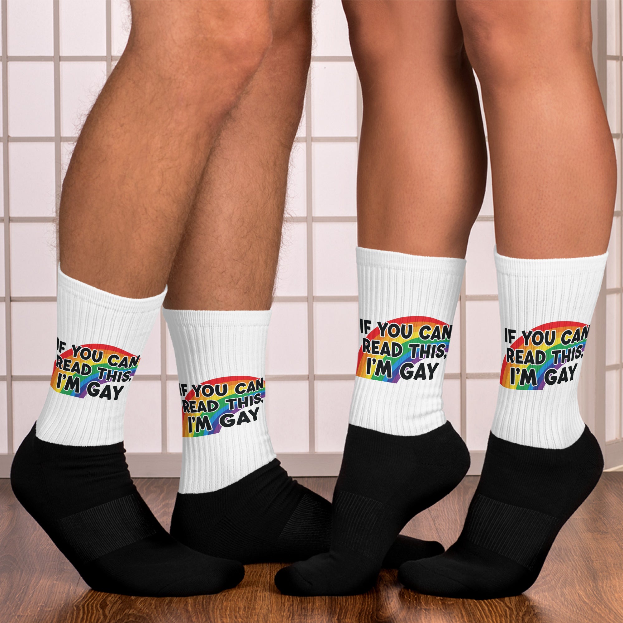 White socks with rainbow text worn by two people on a tiled floor.