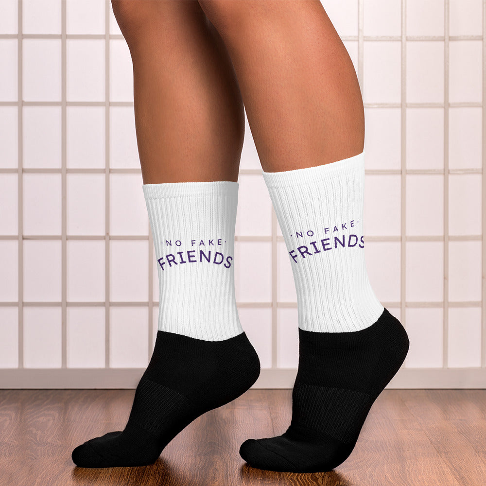 White socks with 'No Fake Friends' text worn by a person on a tiled floor.