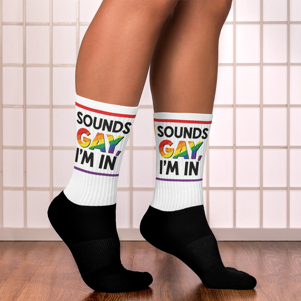 Person wearing socks with 'SOUNDS GAY I'M IN' text and rainbow colors on a tiled floor.