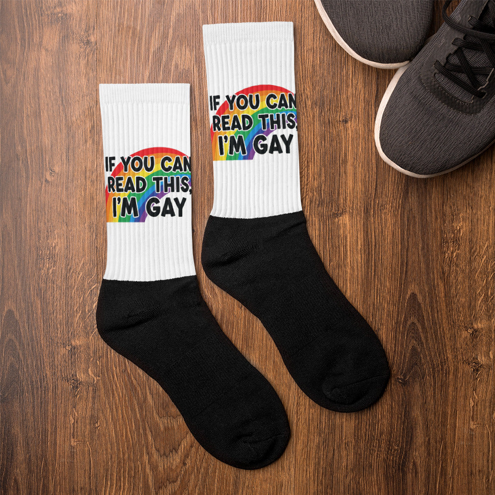 Two socks with rainbow text on a wooden surface next to a shoe.