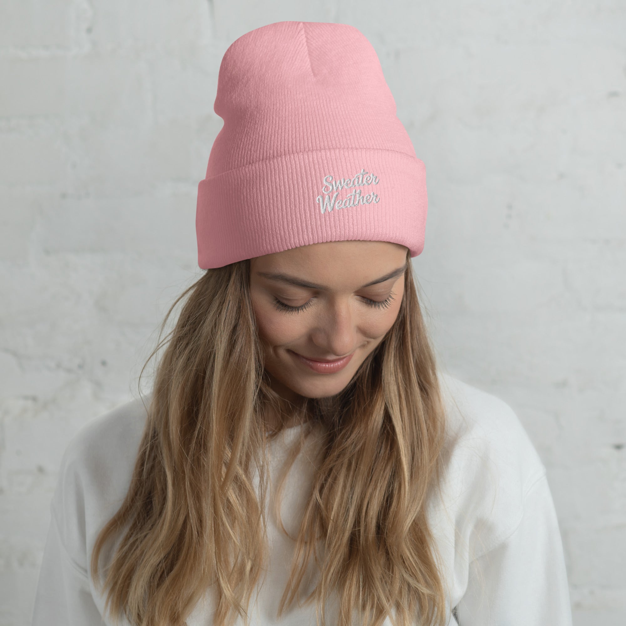 Woman wearing a pink beanie with 'Sweetest Weather' text against a light gray background