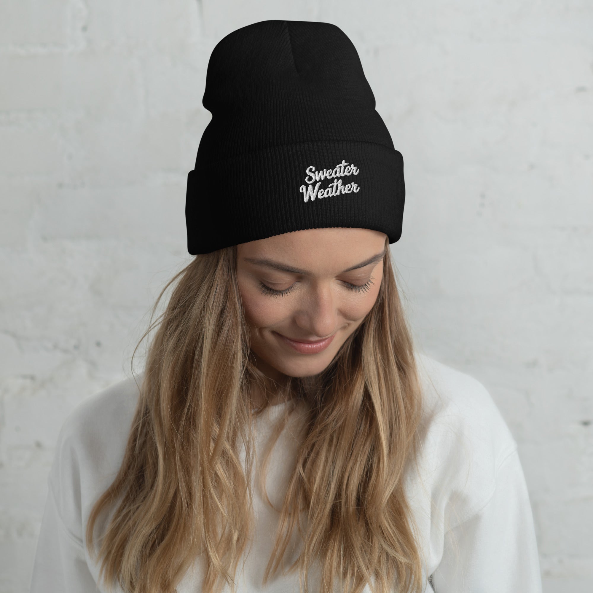 Woman wearing a black beanie with 'Sweater Weather' text against a light gray background