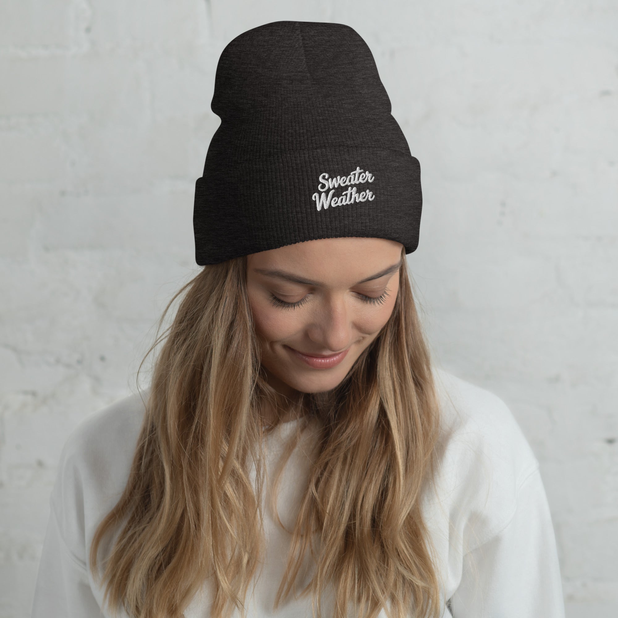 Woman wearing a black beanie with 'Sweater Weather' text against a light gray background