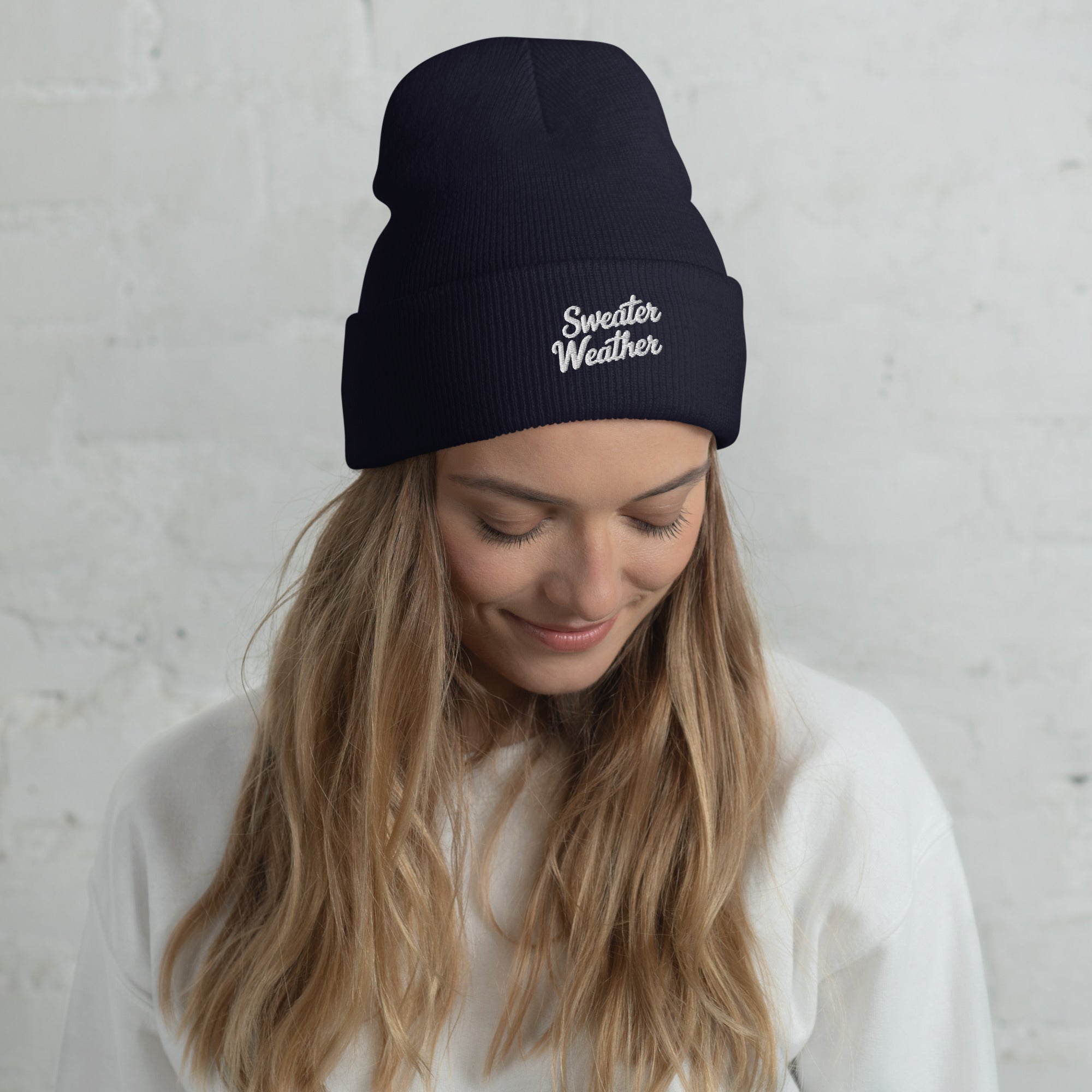Woman wearing a black beanie with 'Sweater Weather' text against a light gray background