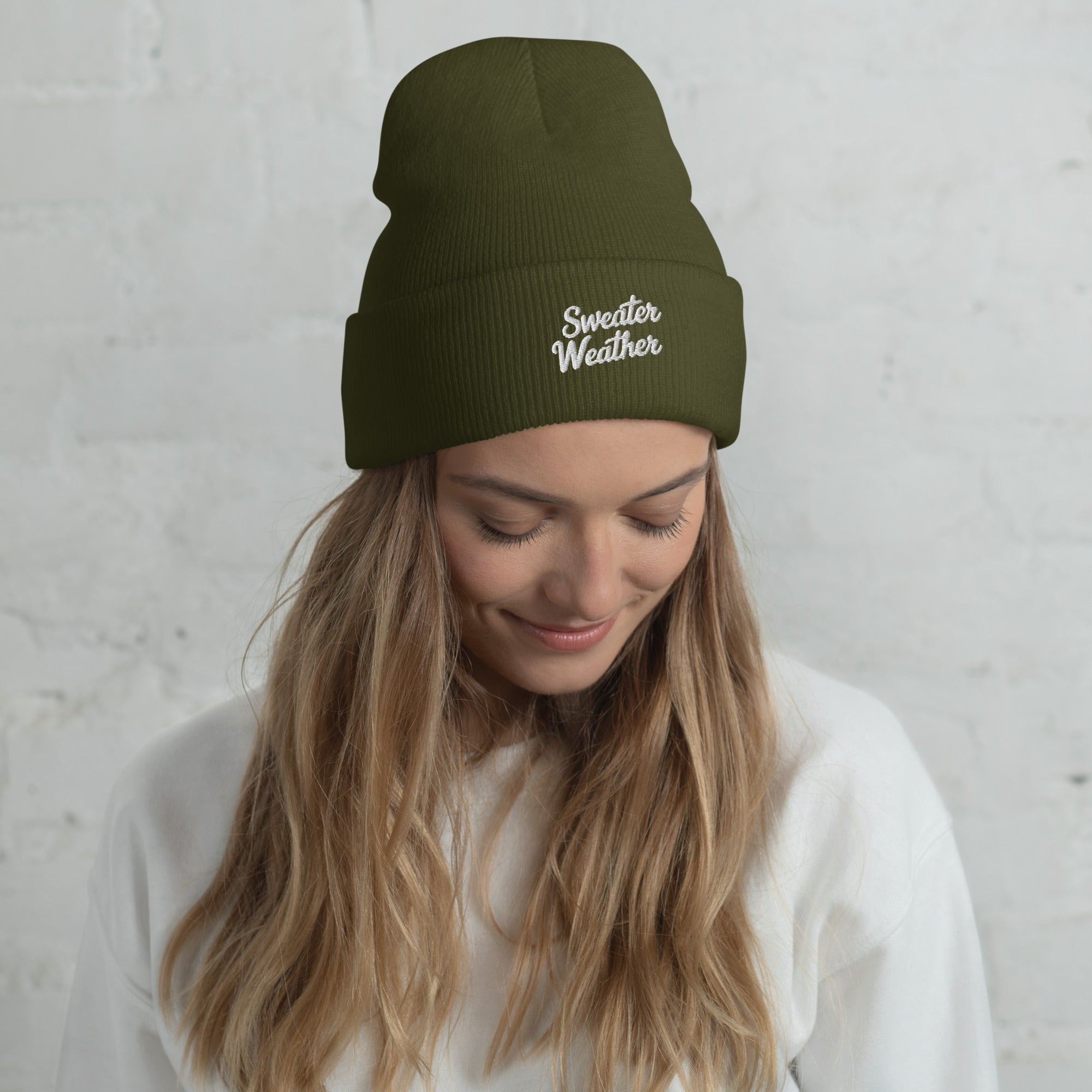 Woman wearing a green beanie with 'Sweater Weather' text against a light gray background