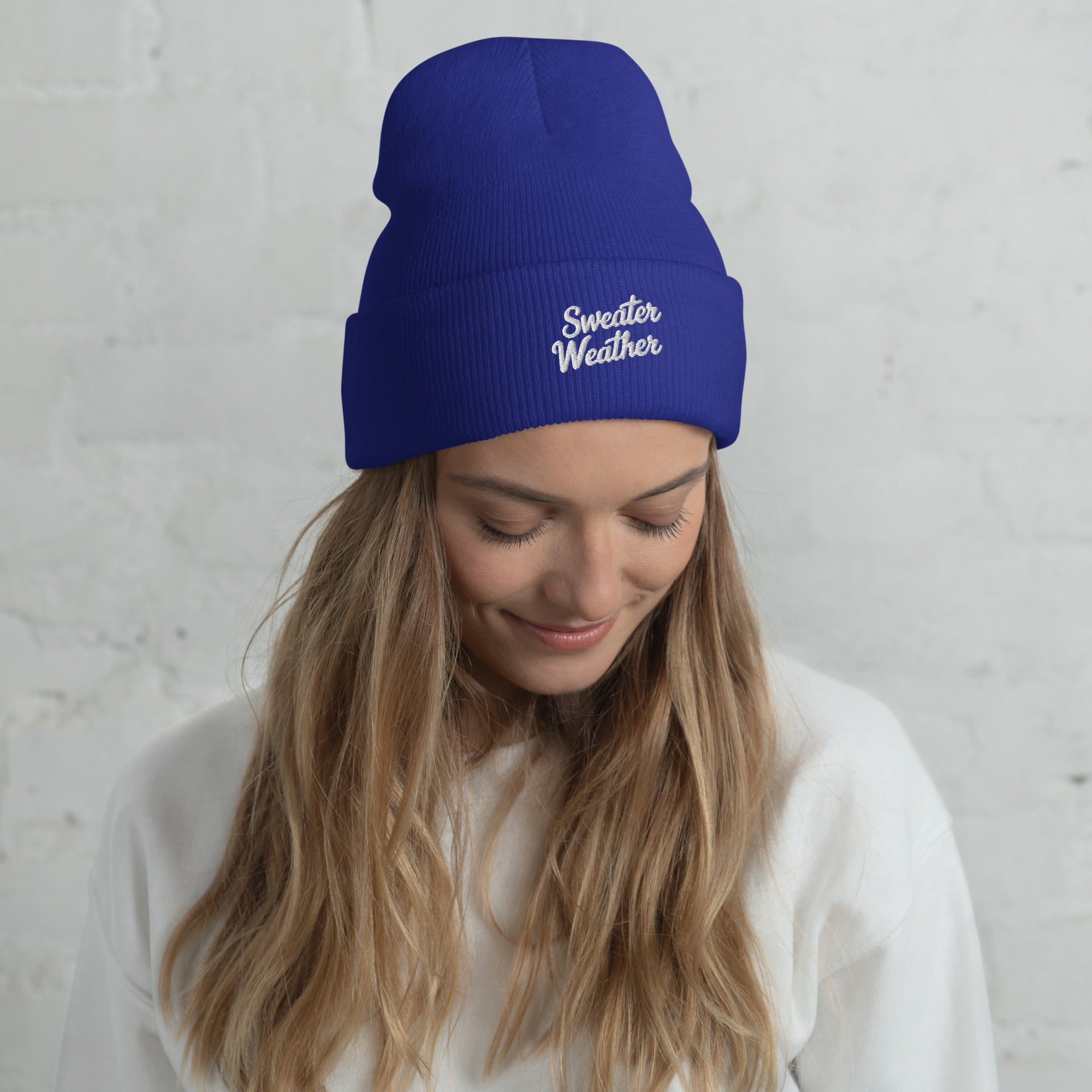 Woman wearing a blue beanie with 'Sweater Weather' text against a light gray background