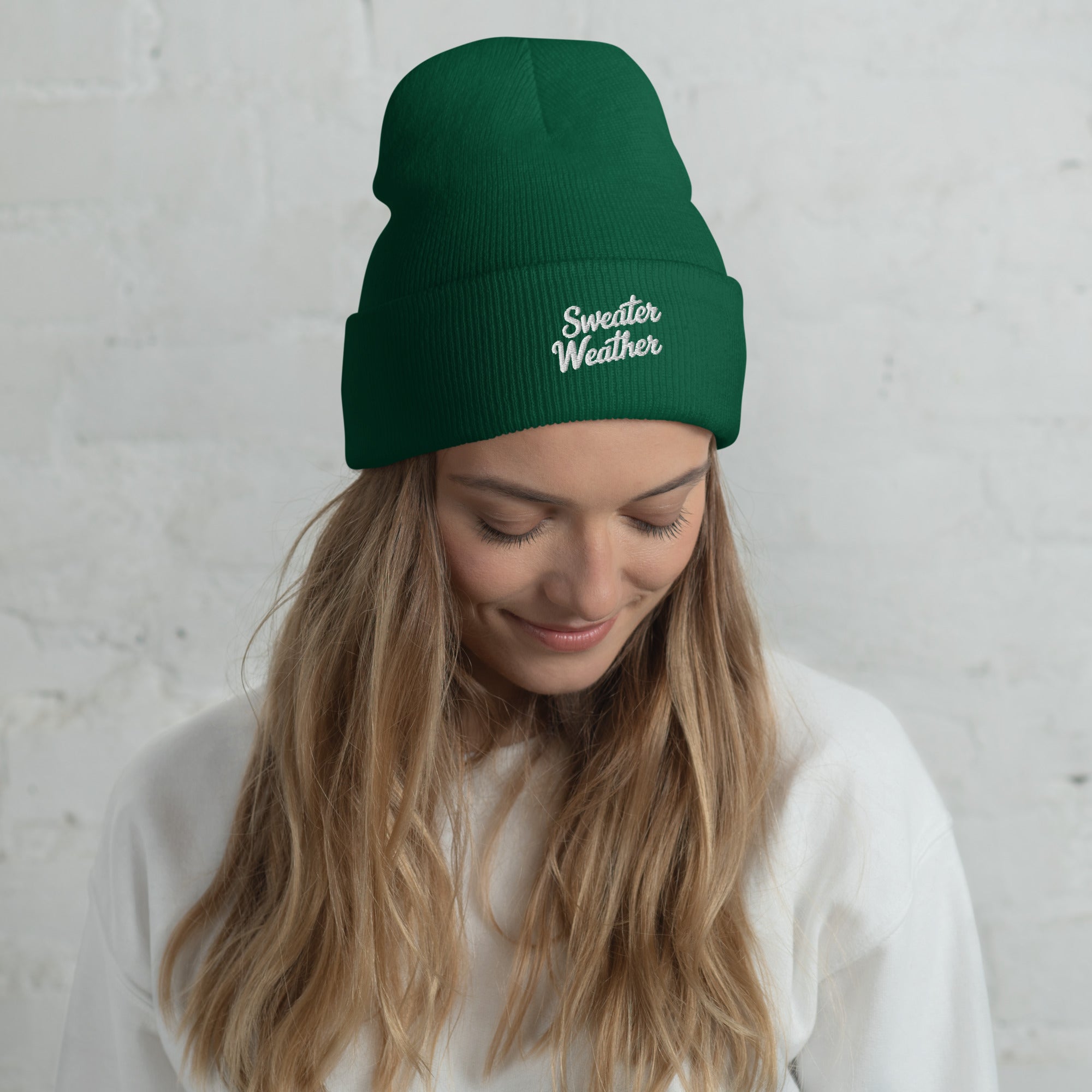 Woman wearing a green beanie with 'Sweater Weather' text against a light gray background