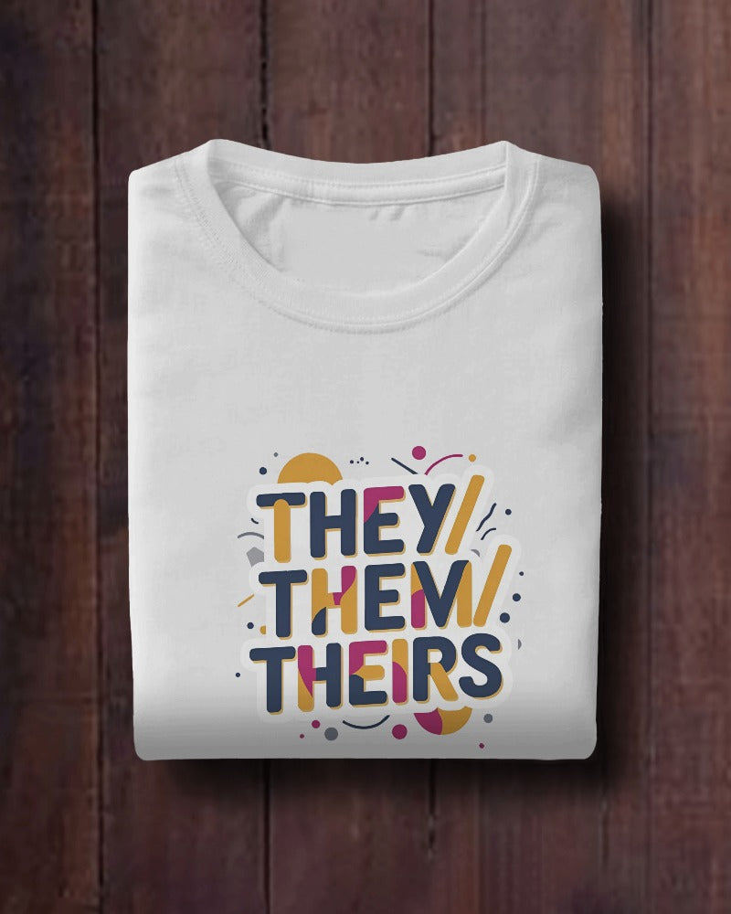 Folded white t-shirt with colorful 'THEY/ THEM/ THEIRS' text on a wooden surface