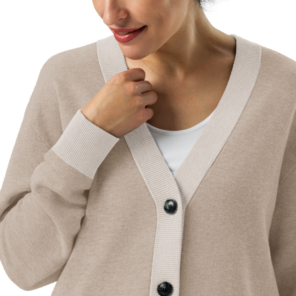 Beige cardigan with black buttons worn by a person on a white background