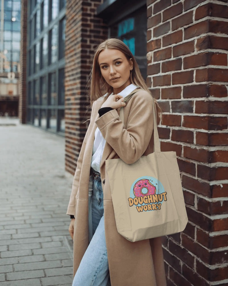 Woman holding a beige tote bag with a doughnut design against a brick wall.