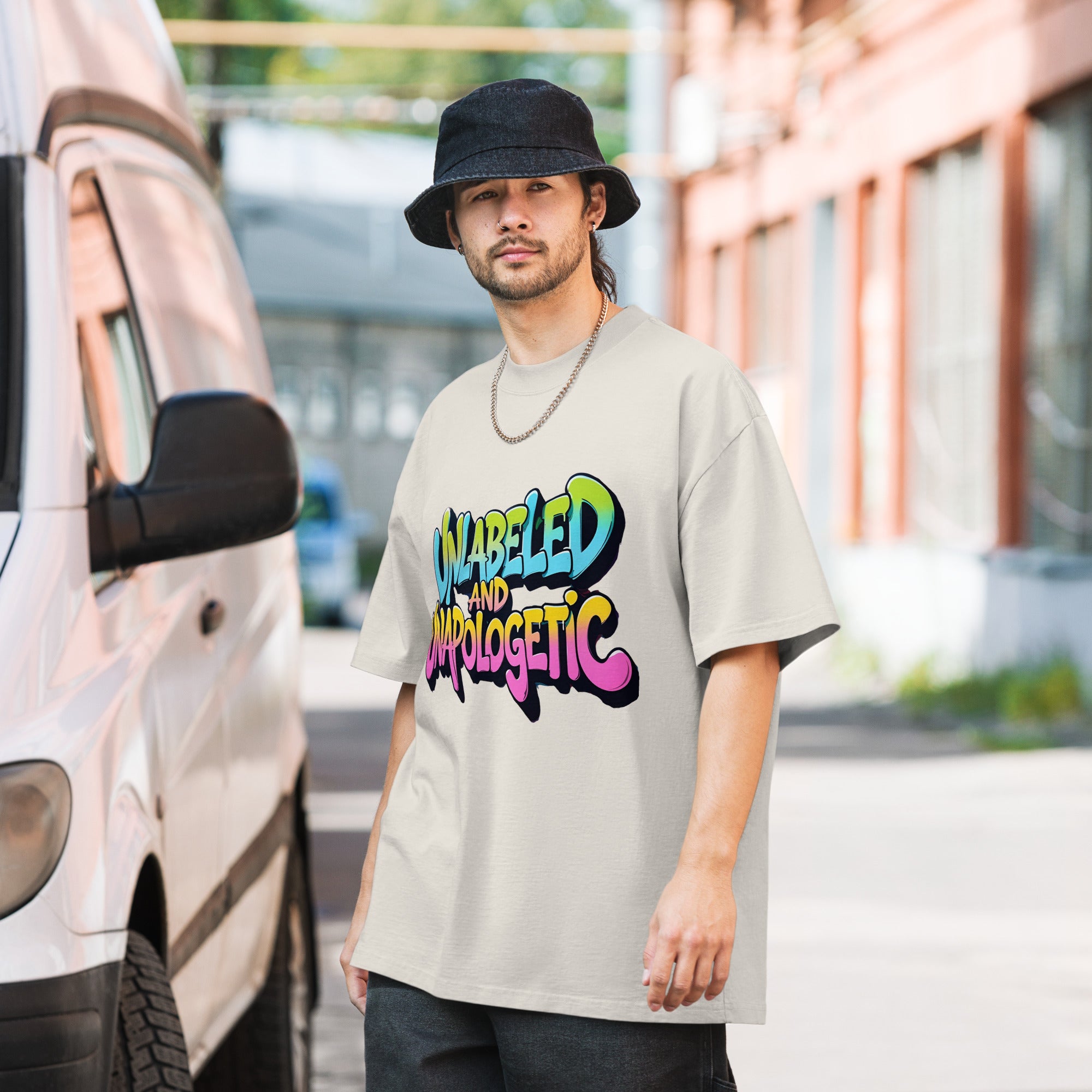 Man wearing a beige t-shirt with colorful text, standing next to a van.