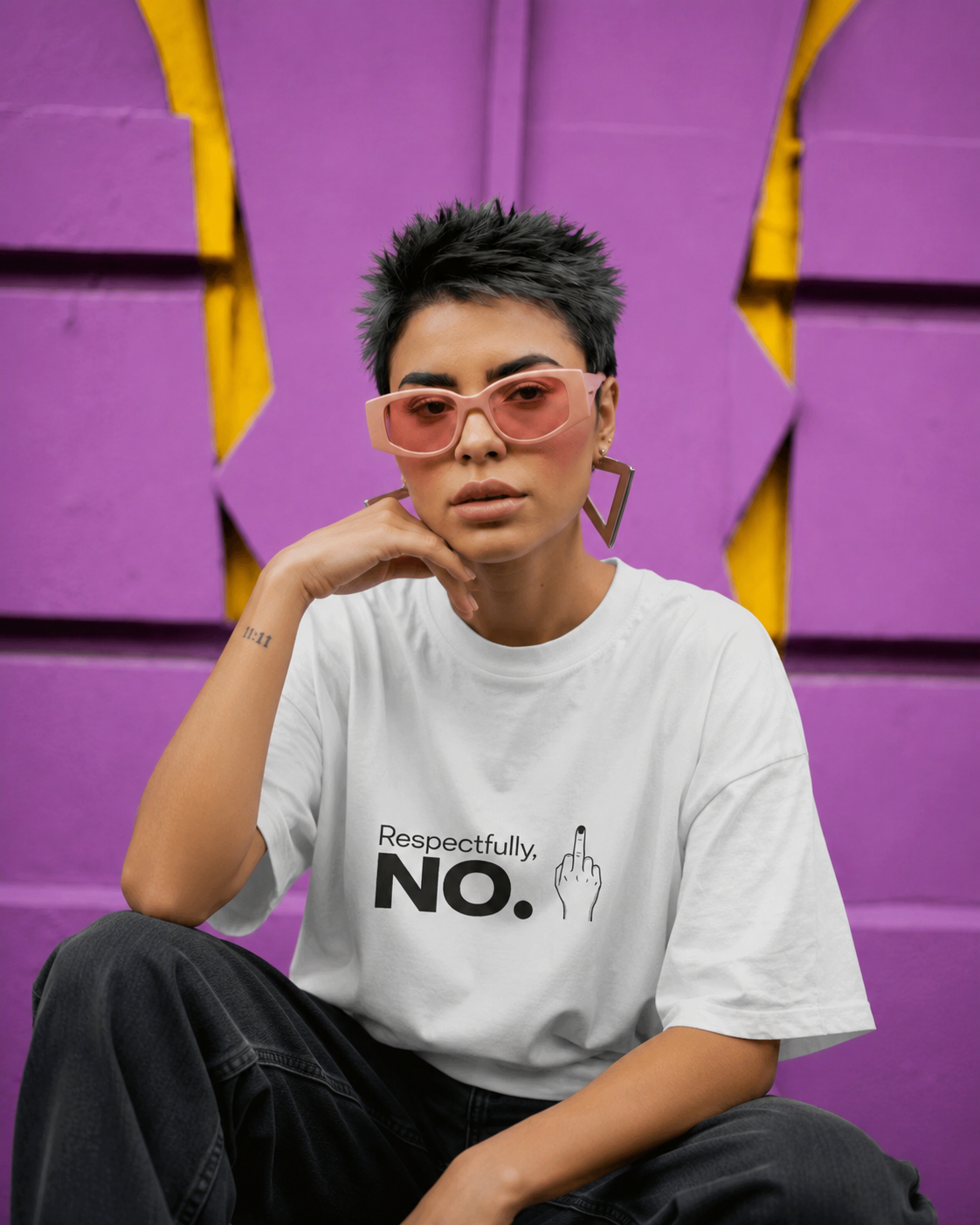 A person wearing a white graphic T-shirt with the text 'Respectfully NO.' and a hand gesture print, seated against a purple and yellow geometric wall.