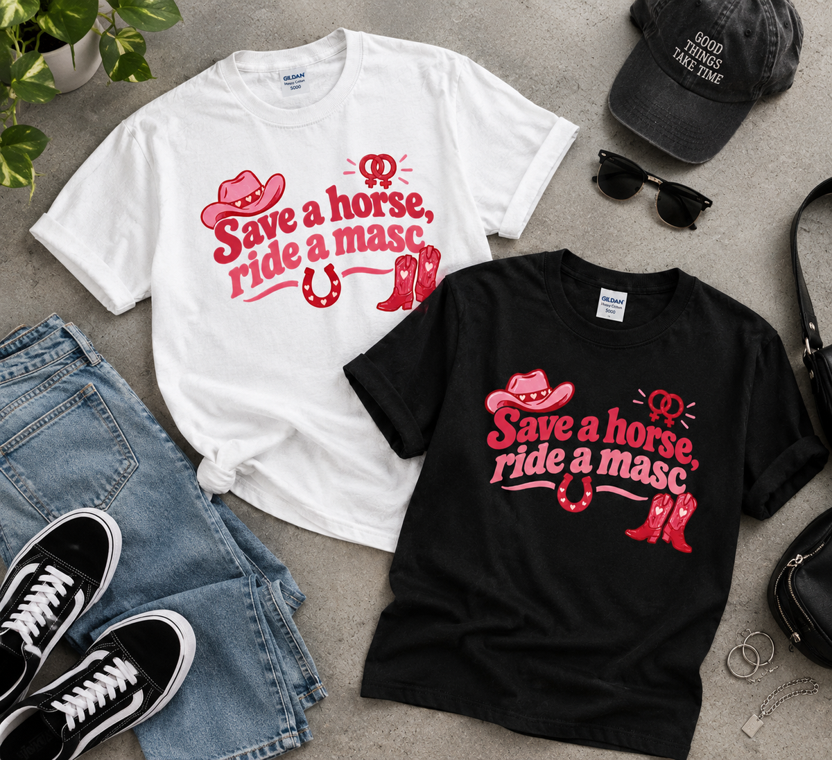 Two graphic T-shirts laid flat on a gray surface, one white and one black, both printed with a red cowboy hat, horseshoe, boots, and the phrase “Save a horse, ride a masc.” Surrounding props include blue jeans, black sneakers, sunglasses, a cap, and a handbag.