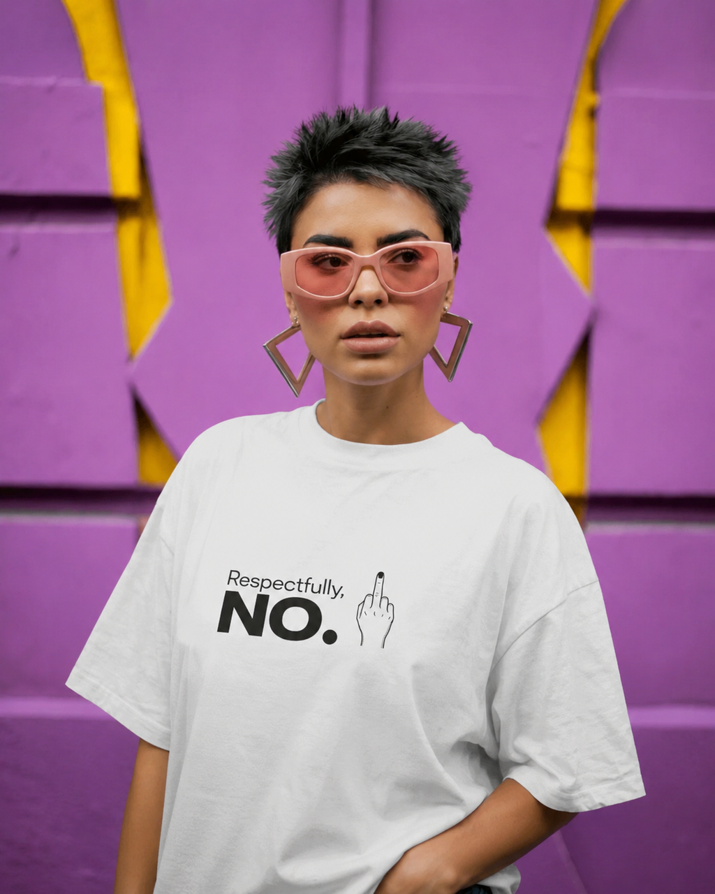A person with short dark hair wearing a white graphic T-shirt that reads 'Respectfully, NO.' with a hand gesture print, pink-tinted sunglasses, and geometric earrings, standing against a purple and yellow wall.
