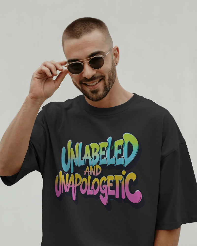 Man wearing a black t-shirt with colorful text 'UNLabeLED AND UNaPOLOGETIC' against a plain background