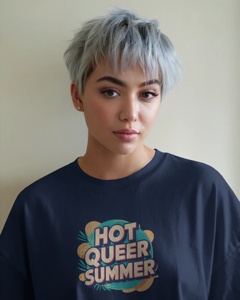 Model wearing Hot Queer Summer slogan T-shirt by Savage Cotton in bright coral, styled with sunglasses and rainbow accessories