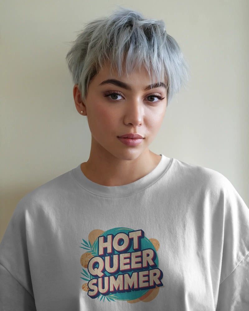 Model wearing Hot Queer Summer slogan T-shirt by Savage Cotton in bright coral, styled with sunglasses and rainbow accessories