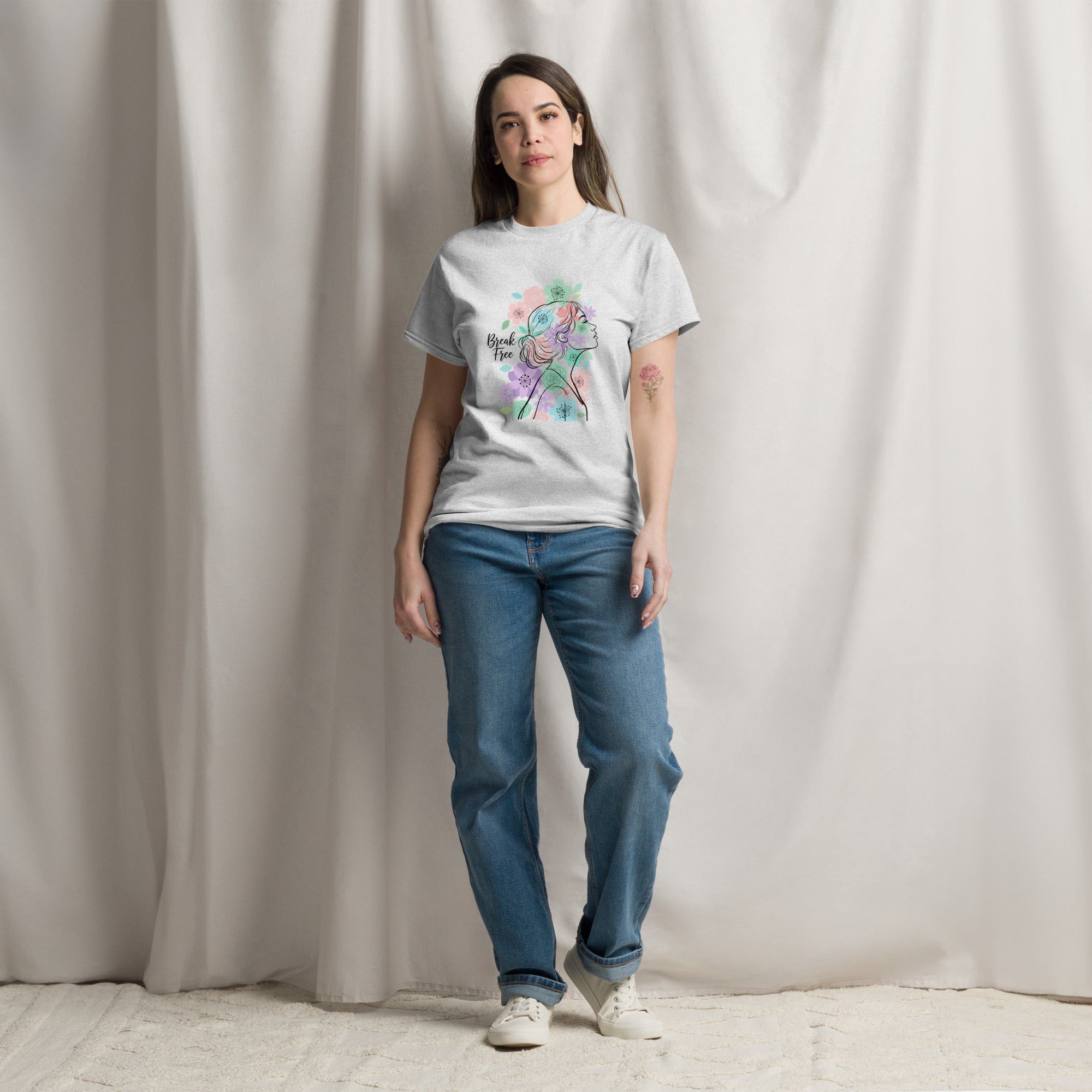 Woman wearing a white t-shirt with a colorful design and blue jeans against a plain background
