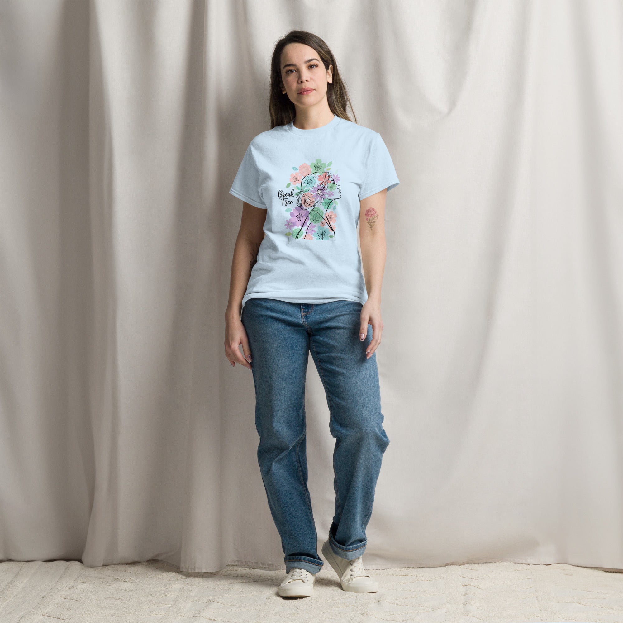 Woman wearing a light blue t-shirt with a floral design and blue jeans against a plain background