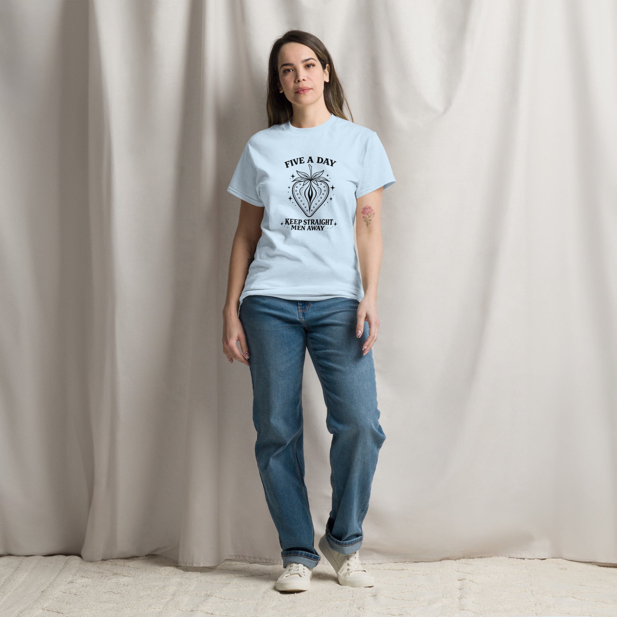 Woman wearing a light blue t-shirt with a graphic design and blue jeans against a plain background