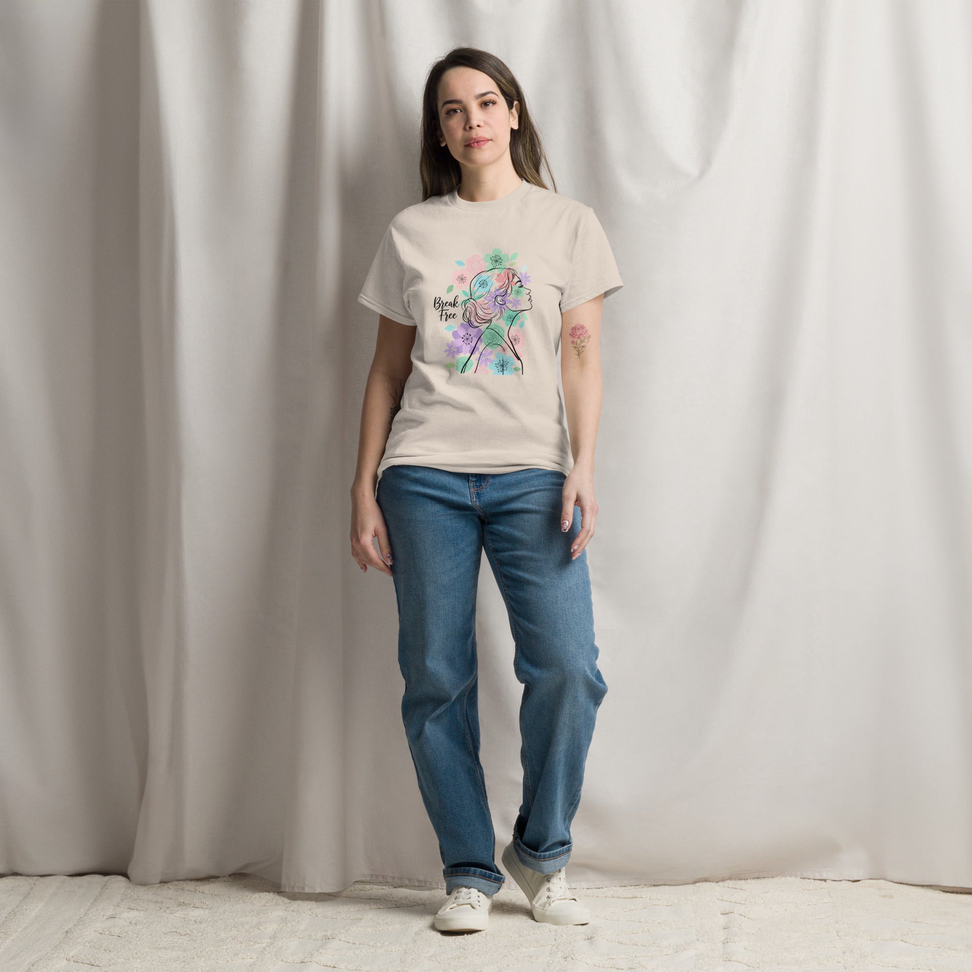 Woman wearing a beige t-shirt with a colorful graphic and blue jeans against a plain background