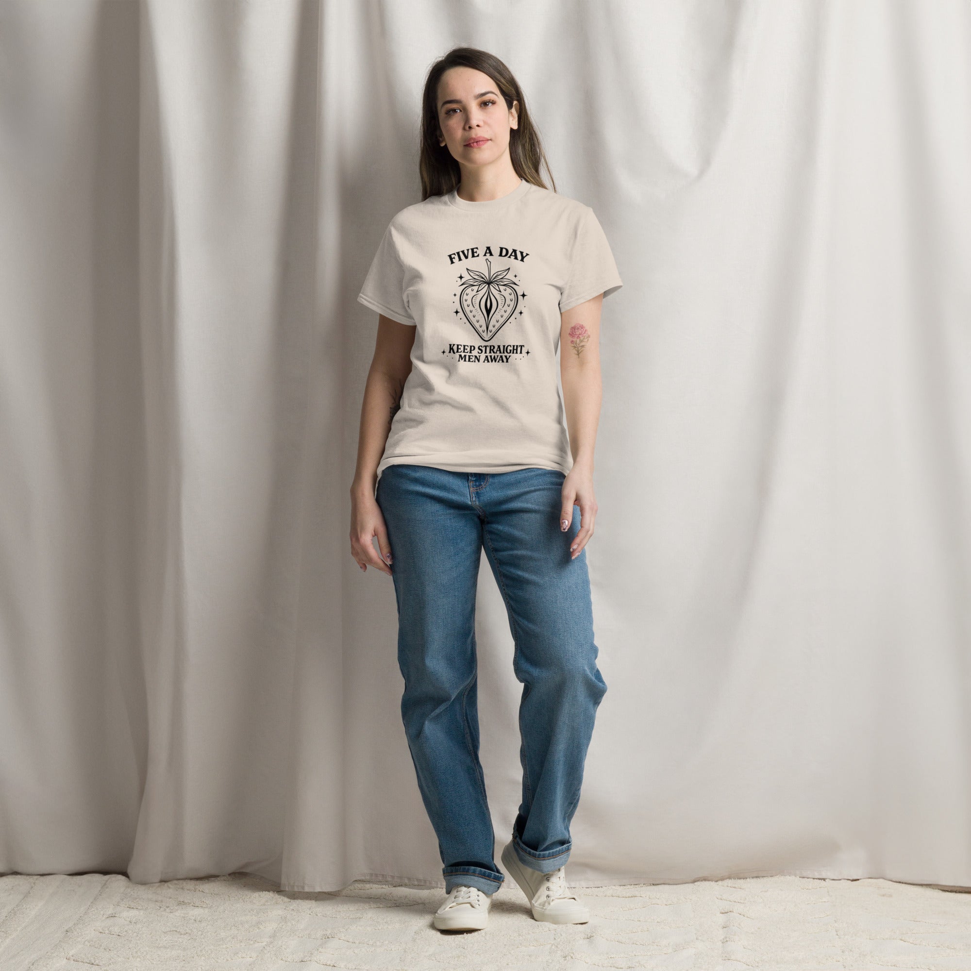 Woman wearing a beige t-shirt with a pattern and blue jeans against a plain background