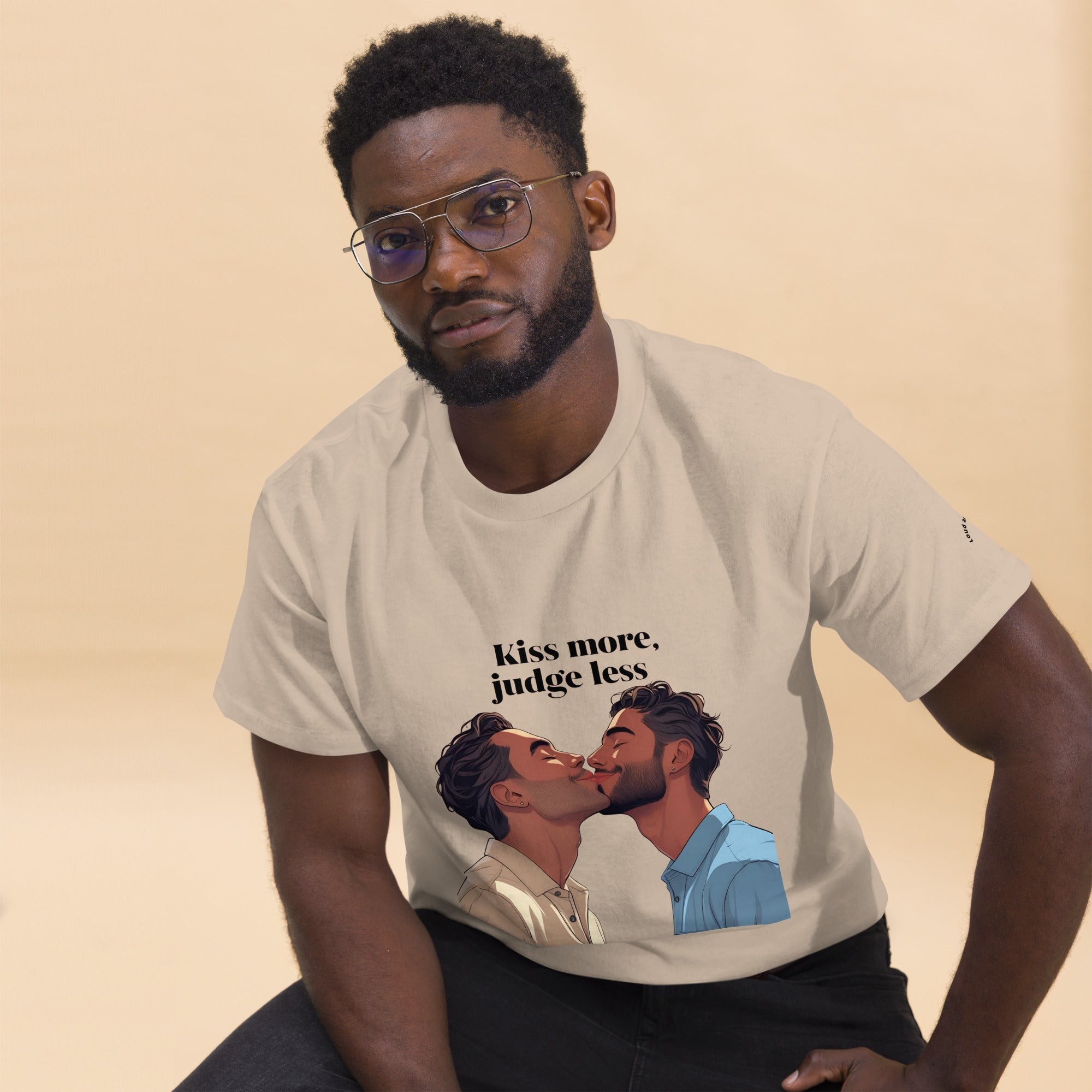 Man wearing a t-shirt with a graphic of two people kissing and text 'Kiss more, judge less' on a beige background.