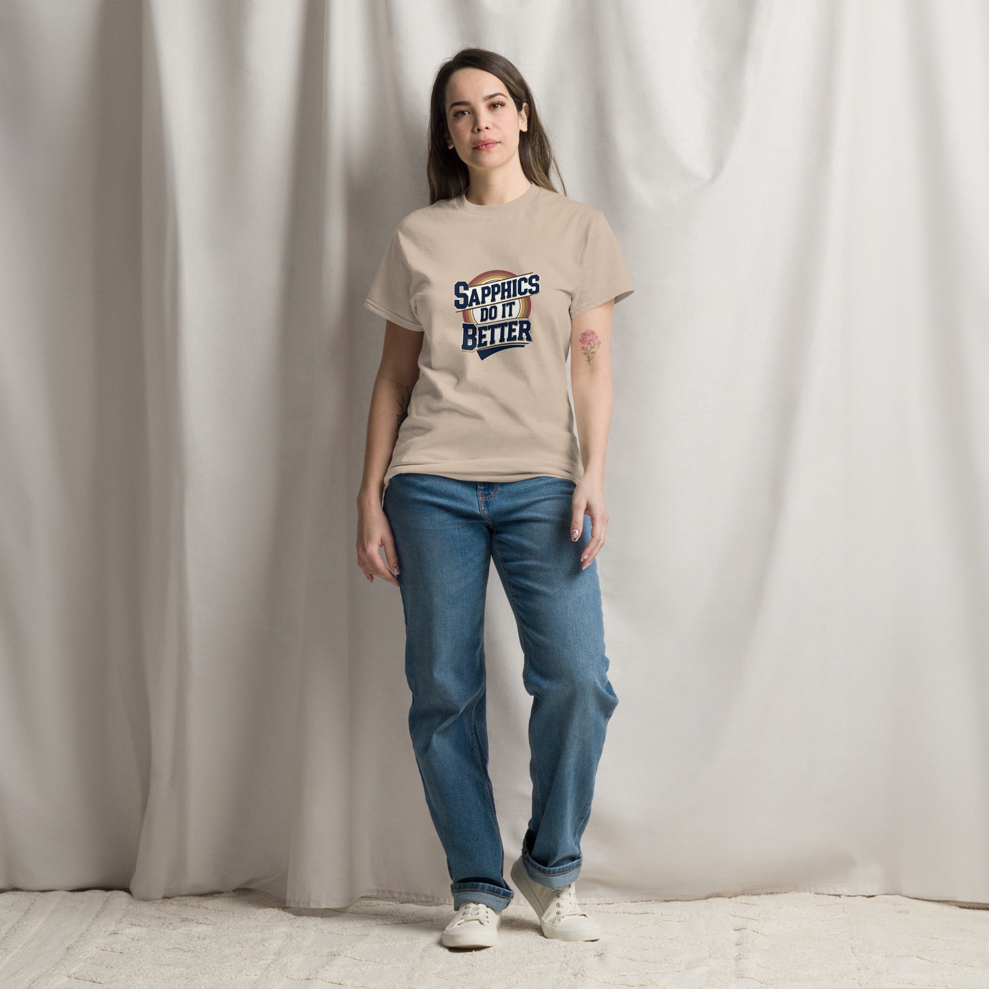Person wearing a beige t-shirt with text and blue jeans standing against a plain background