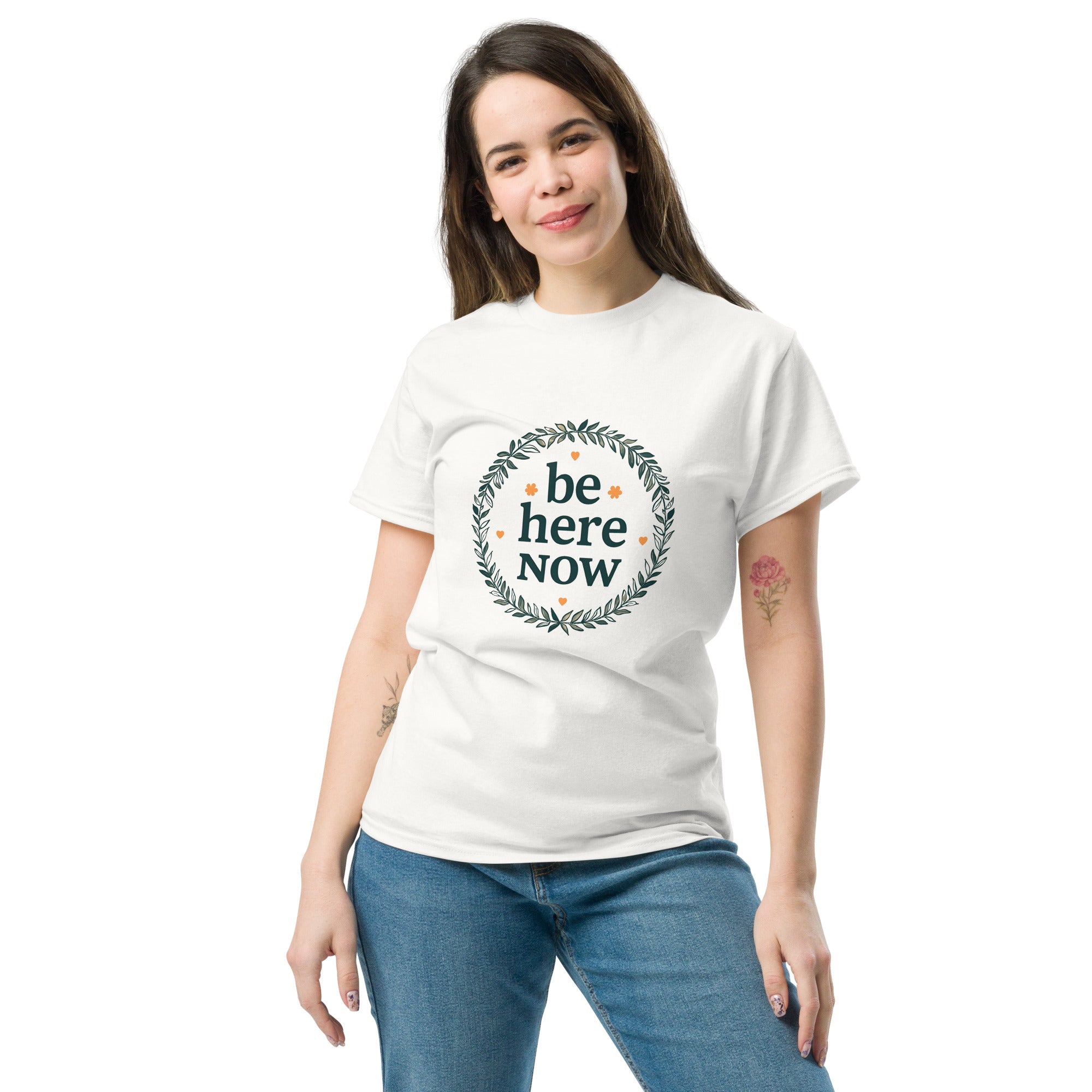 Woman wearing a white t-shirt with 'be here Now' text on a plain background