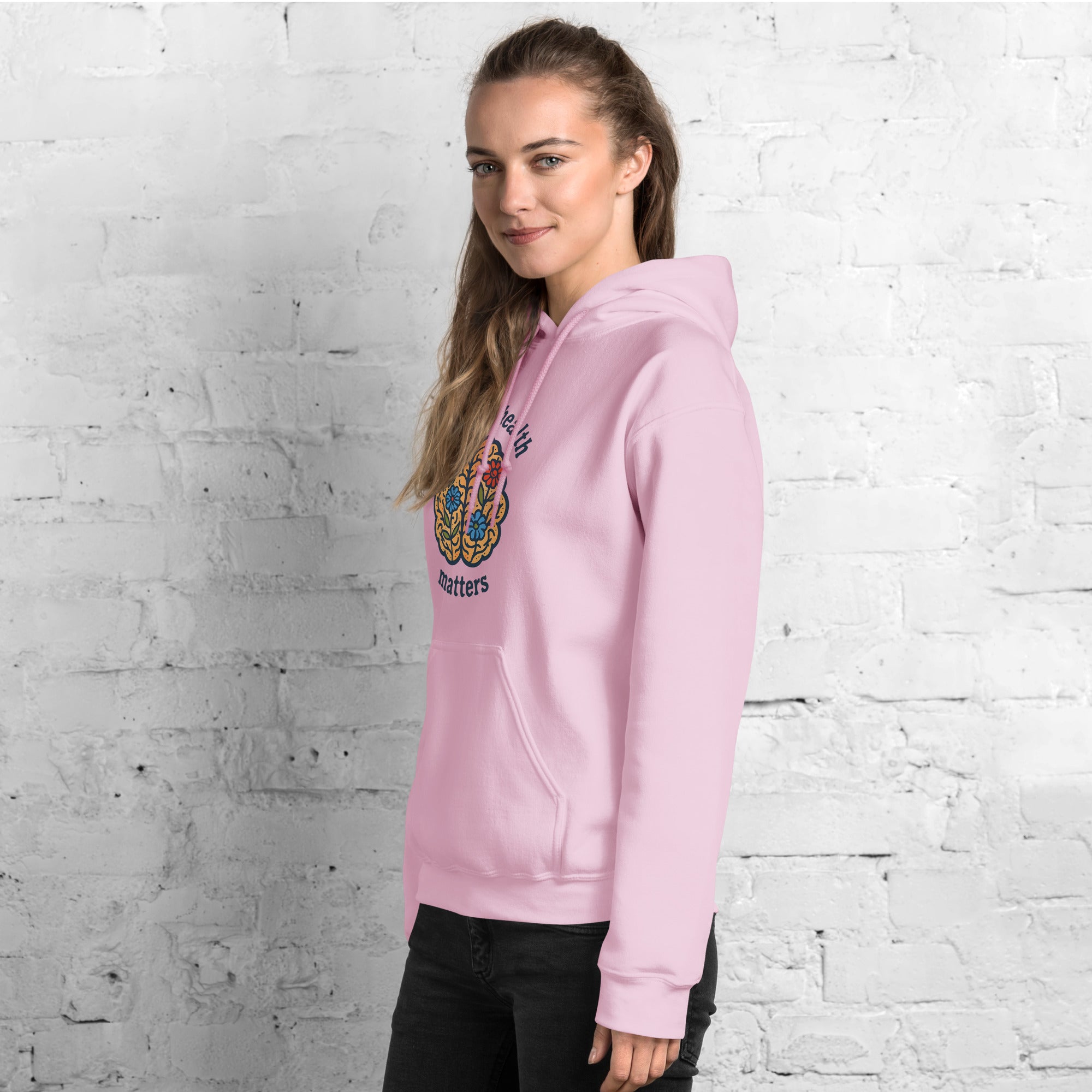 Person wearing a pink hoodie with a colorful logo against a white brick wall.