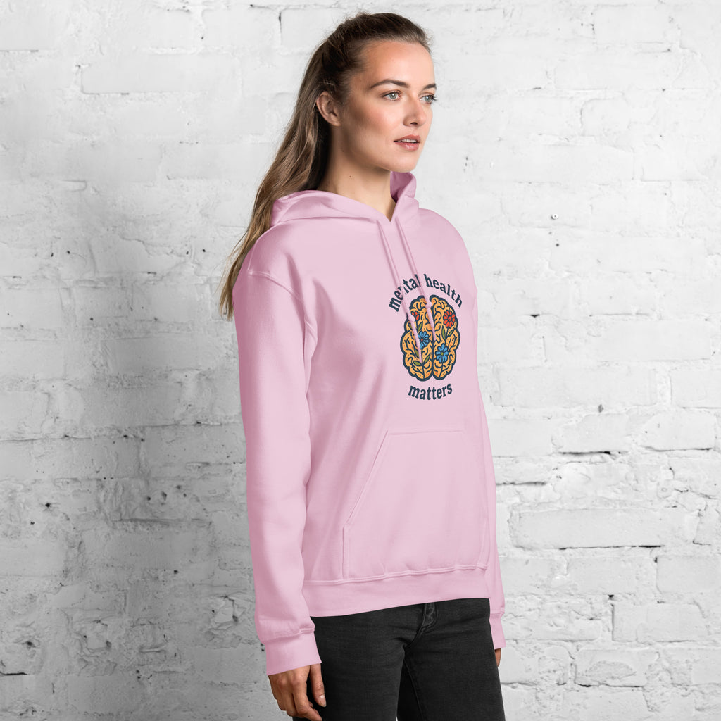Person wearing a pink hoodie with 'mental health matters' text and design against a white brick wall.
