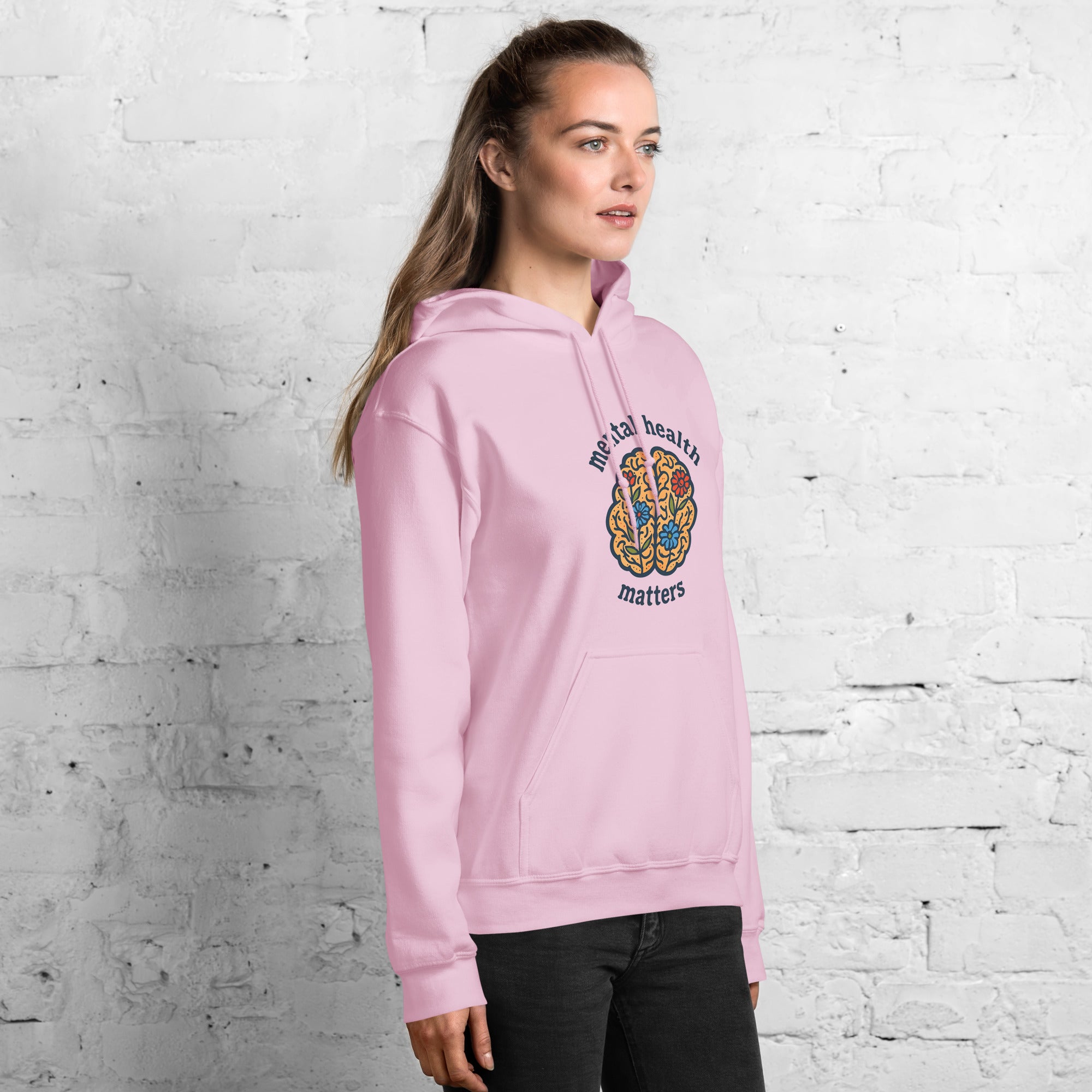 Person wearing a pink hoodie with 'mental health matters' text and design against a white brick wall.