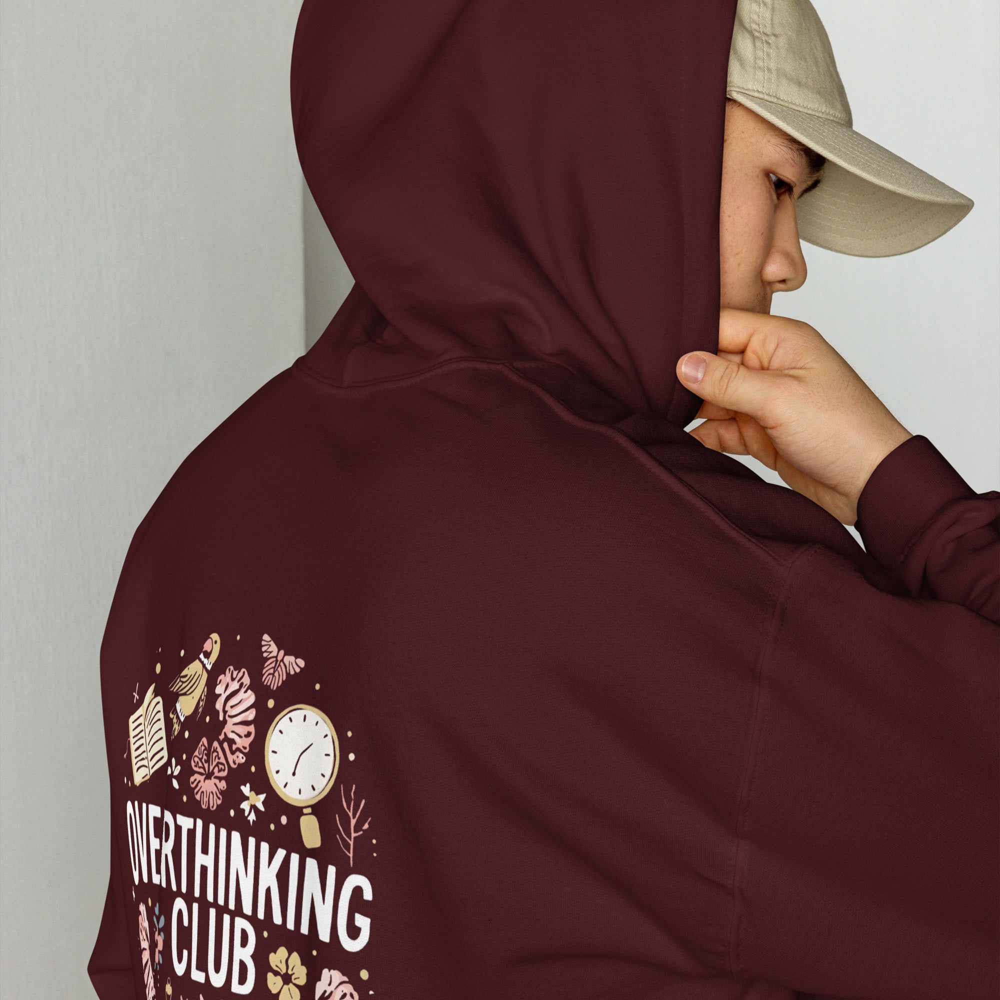 Person wearing a maroon hoodie with 'Overthinking Club' text and graphics, covering their face.