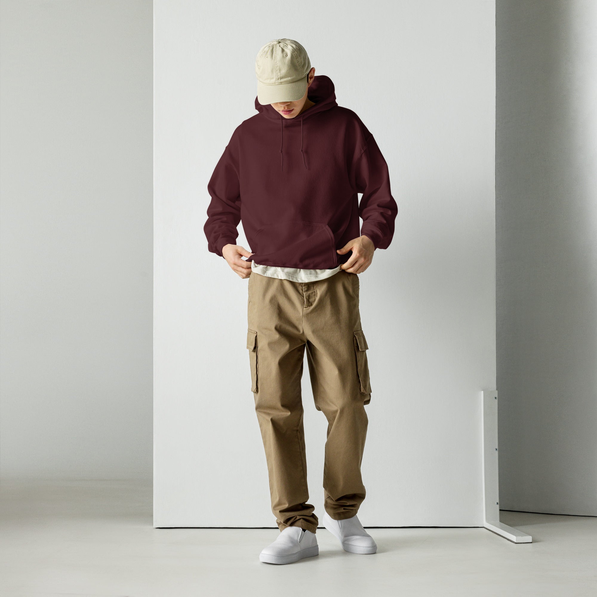 Person wearing a maroon hoodie, beige cap, and brown cargo pants against a white background
