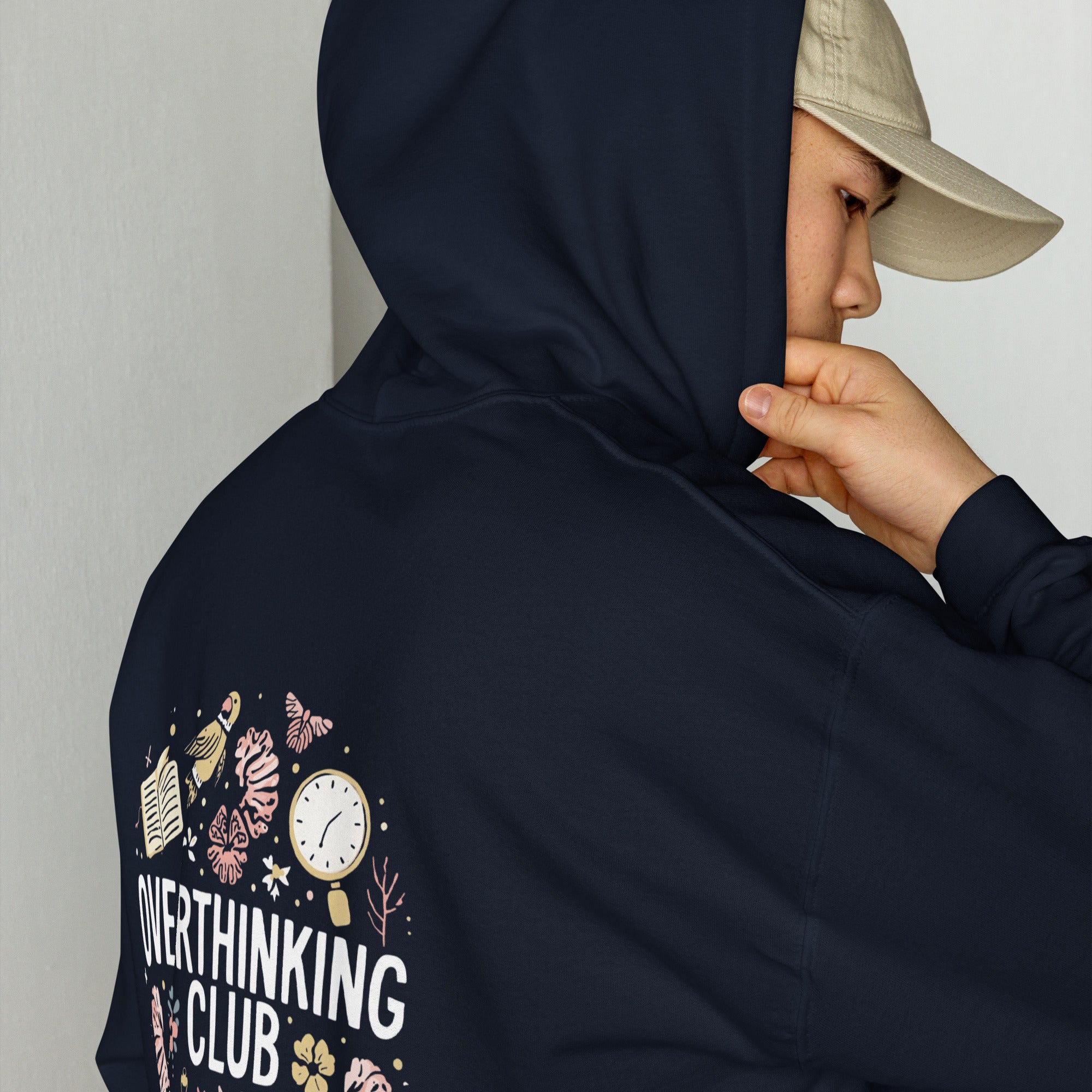 Person wearing a navy hoodie with 'Overthinking Club' design, leaning against a light-colored wall.