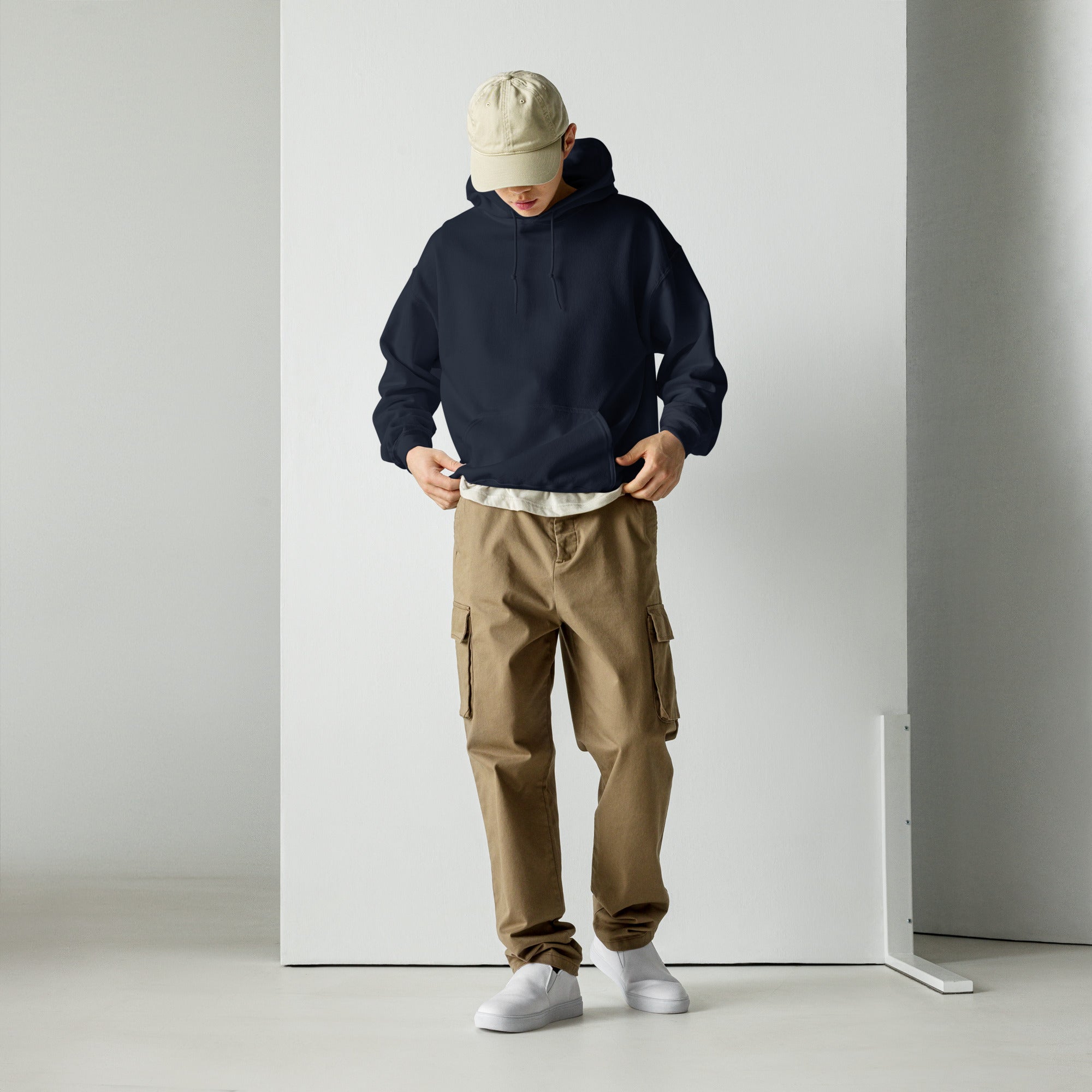 Person wearing a navy hoodie, beige cap, brown cargo pants, and white shoes against a plain background