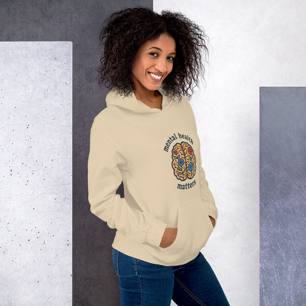 Woman wearing a beige hoodie with a colorful design and text against a gray and white background