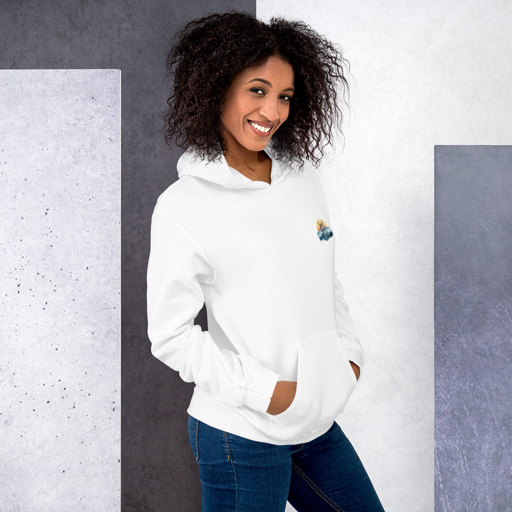 Woman wearing a white hoodie and blue jeans standing against a gray and white wall.