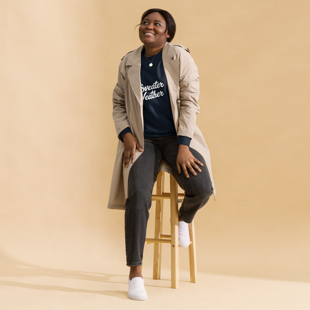 Woman sitting on a stool wearing a trench coat over a graphic t-shirt with text, on a beige background